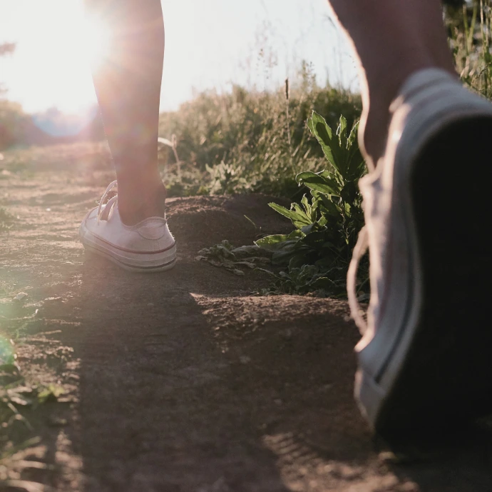 voeten wandelen over zanderig pad met zonlicht op achtergrond