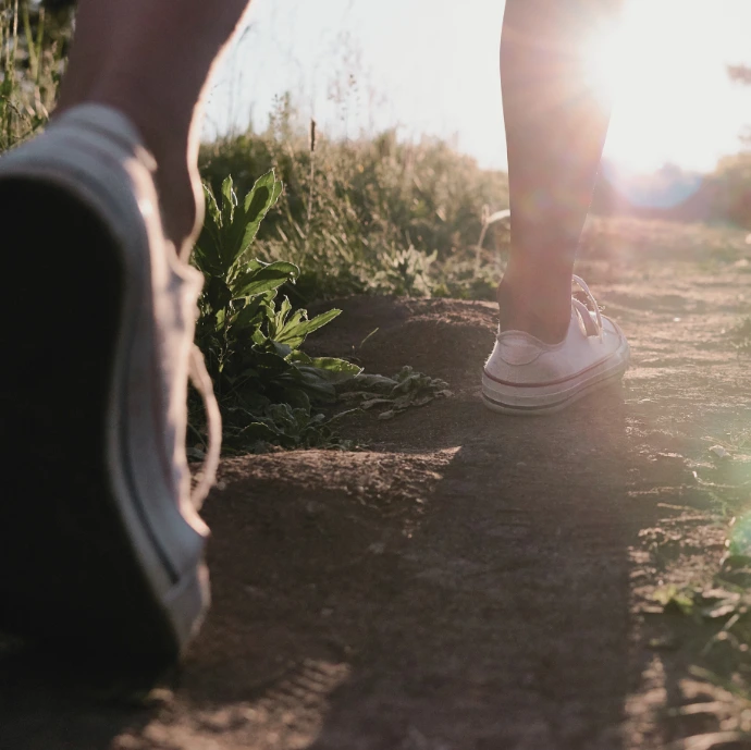 voeten wandelen over zanderig pad met zonlicht op achtergrond
