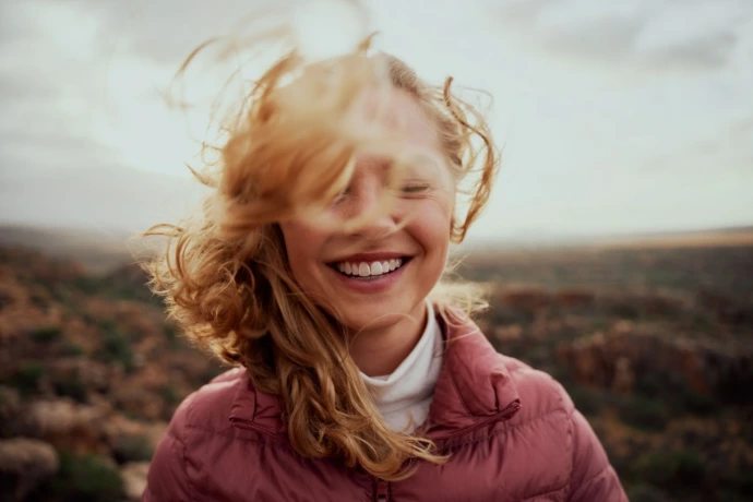 jonge vrouw met lach op gezicht en wind in haren buiten